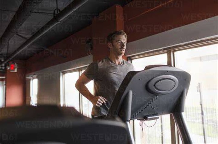 exhausted mid adult man running uphill on gym treadmill