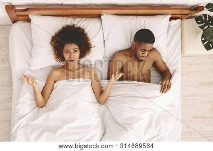 Upset pair of lovers lying on the bed. Family conflict. sex problem disappointed black unsatisfied woman lying in bed, sad man looking under blanket, top view